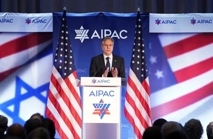 An image of US Secretary of State Antony Blinken standing on a podium at AIPAC, flanked by two American flags and with the AIPAC logo behind him.